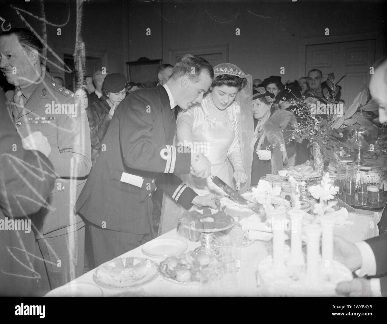 ADMIRAL'S SON WEDS EARL'S DAUGHTER. 10 FEBRUARY 1944, ADMIRALTY HOUSE. AT THE RECEPTION ATTENDED BY PRINCESS ELIZABETH AND PRINCESS MARGARET, WHICH FOLLOWED THE WEDDING AT WESTMINSTER ABBEY OF LIEUTENANT CHRISTOPHER WAKE-WALKER, RN, SON OF VICE ADMIRAL SIR FREDERICK AND LADY WAKE-WALKER, AND THIRD OFFICER LADY ANNE SPENCER, WRNS, DAUGHTER OF EARL AND COUNTESS SPENCER. - The bride and groom cutting the cake. , Wake-Walker, Christopher Baldwin Hughes, Spencer, Anne Stock Photo