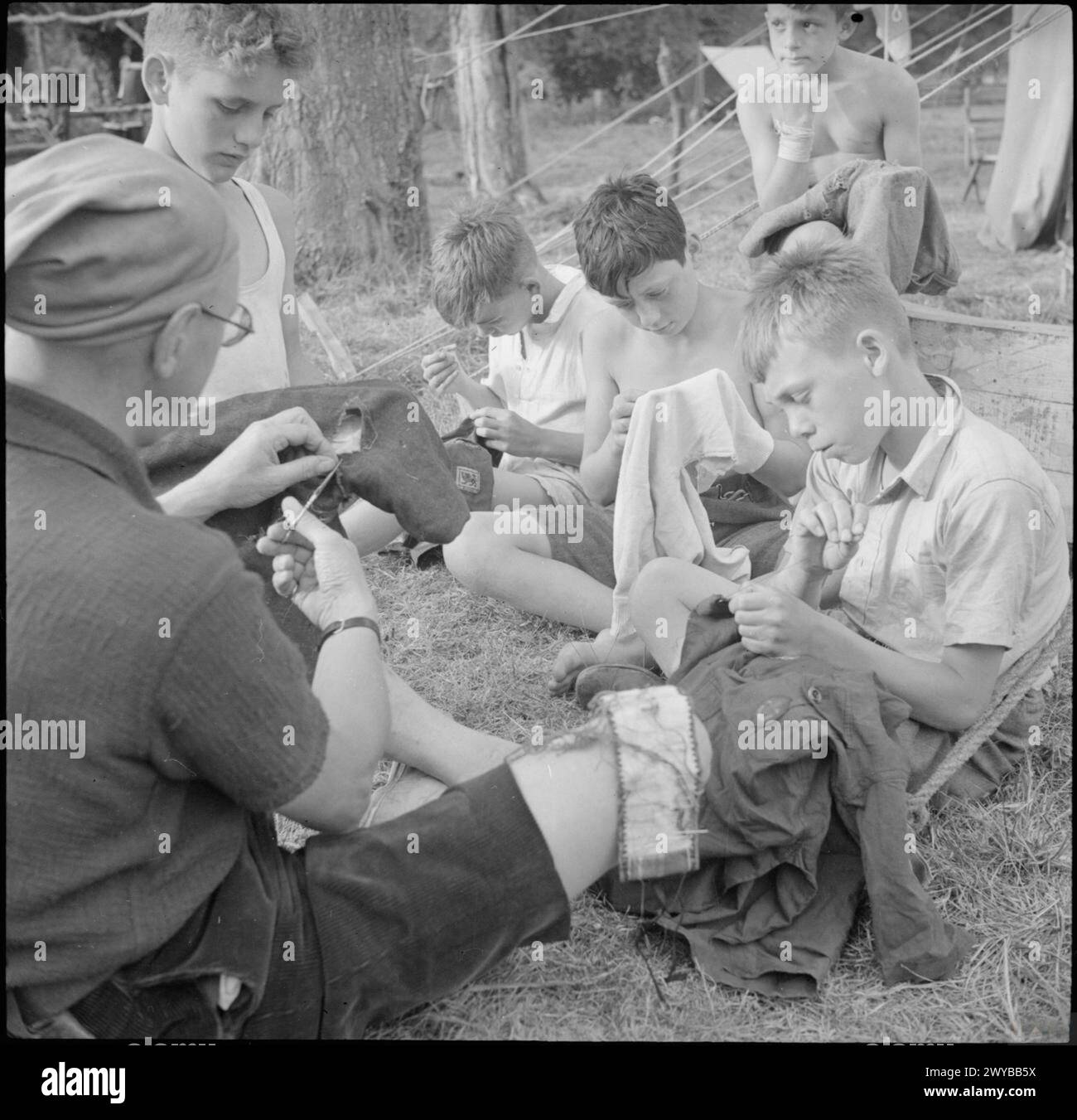 A small group of Boy Scouts repair clothing with the help of a Scout ...