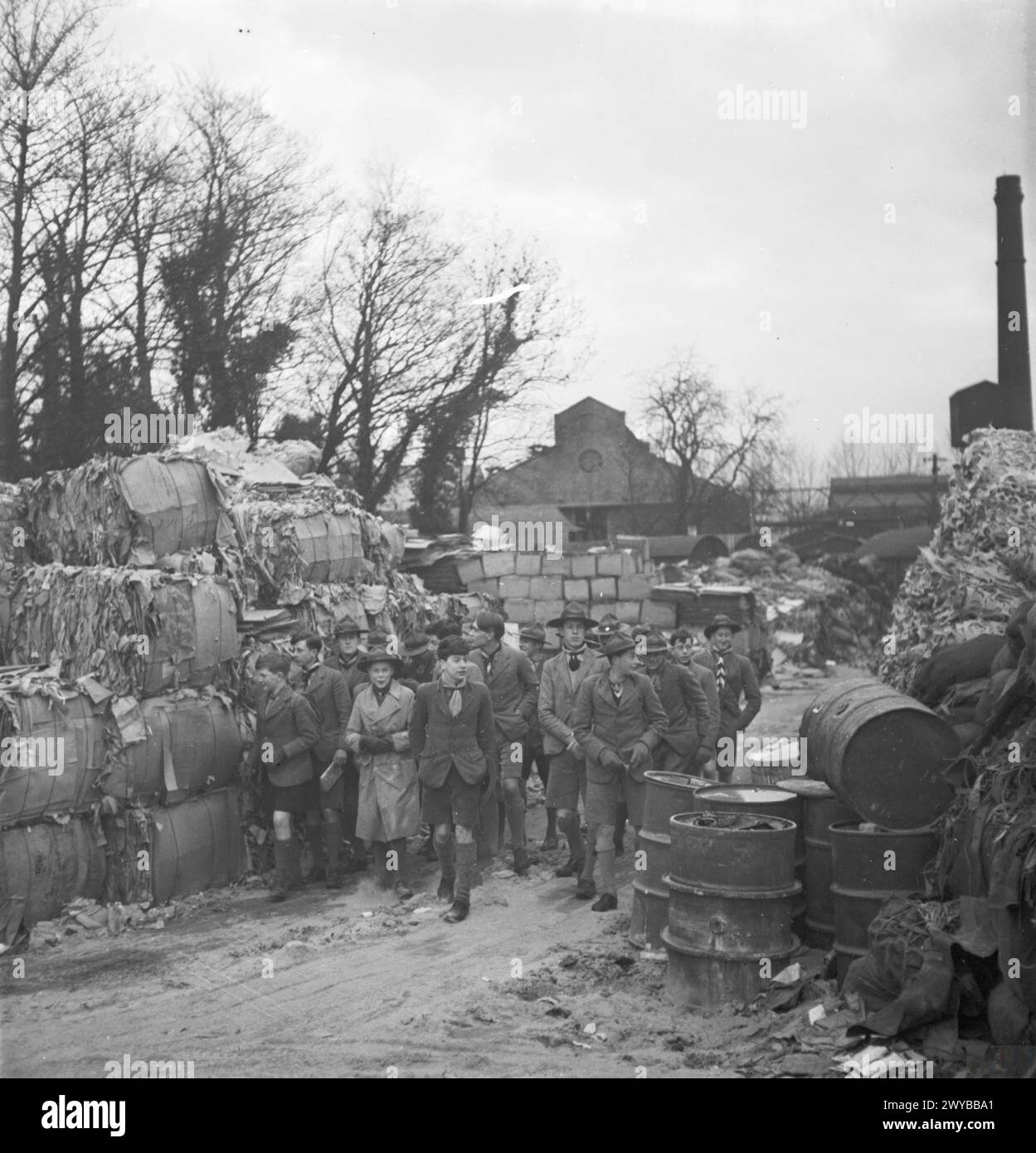 SALVAGE IN WARTIME BRITAIN: BOY SCOUTS VISIT A PAPER MILL, UK, 1943 - A group of Boy Scouts from Eton College walk between piles of salvaged materials during their visit to a paper mill, somewhere in Britain. Members of the Boy Scout Movement played a huge part in the paper salvage campaigns across the country during the War. , Stock Photo