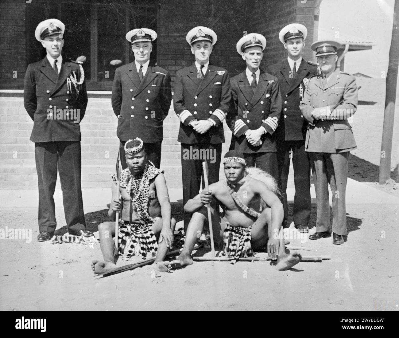 ZULU PRESENTATION TO HMS ASSEGAI. 21 SEPTEMBER 1943, ZULU'S PARADISE, POCO POCO LAND. THE PRESENTATION BY ZULU CHIEFTAINS TO HMS ASSEGAI OF A ZULU SHIELD, ASSEGAIS (A SLENDER IRON TIPPED LANCE OR JAVELIN), A KNOBKERRIE AND OTHER WEAPONS. THE PRESENTATION WAS MADE TO REAR ADMIRAL R J R SCOTT, AM, AND INCLUDED AN ILLUMINATED ADDRESS IN ZULU. - The Zulu Chiefs and their gifts with, (left to right) Paymaster Lieutenant Commander D C Woolf, RN, Commander K W Stewart, RN, Rear Admiral R J R Scott, AM, Captain B E Adams, DSO, RN, Sub Lieutenant O W Dyers, SANF (V), Major A J Smart, Commandant South A Stock Photo