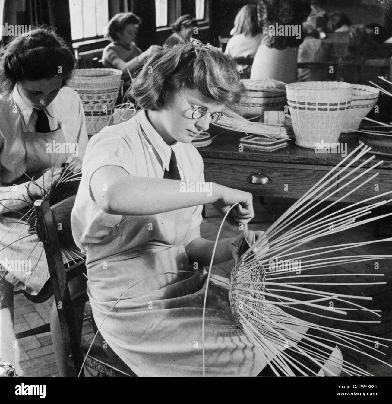 COUNTRY SCHOOL: EVERYDAY LIFE AT BALDOCK COUNTY COUNCIL SCHOOL, BALDOCK, HERTFORDSHIRE, ENGLAND, UK, 1944 - A group of girls busy at work during a lesson on basket-making at Baldock County Council School. They are weaving the wicker strands to make waste paper baskets. , Stock Photo