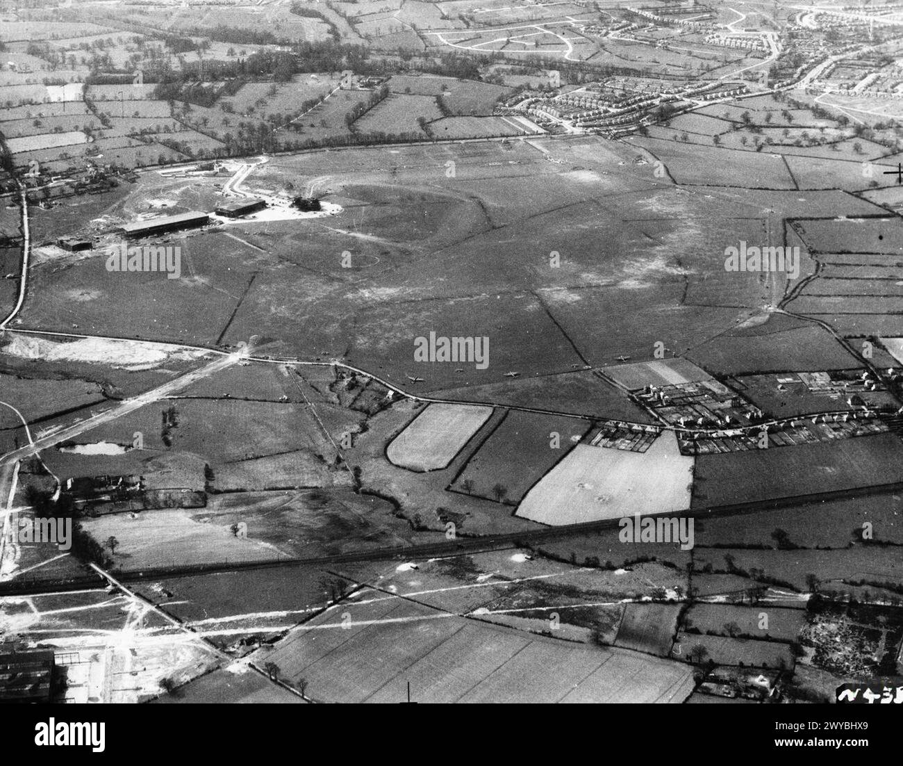 ROYAL AIR FORCE FLYING TRAINING COMMAND, 1940-1945. - Oblique aerial view of RAF Elmdon, Warwickshire, seen from the north-west. A broad concrete taxiway (lower left) leads from the Austin Motors Ltd assembly sheds (partly visible at bottom left), under the Coventry-Birmingham railway line, to the airfield perimeter. Short Stirlings (and, later, Avro Lancasters) built at Austin's Longbridge plant were assembled here and tested at Elmdon before their delivery flights. Note the attempt to camouflage the grass airfield with a field pattern and hedegrows. , Royal Air Force, 1 Camouflage Unit Stock Photo