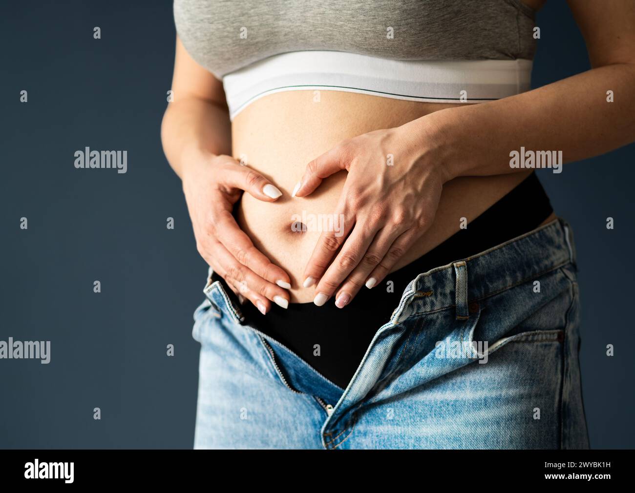Stomach of pregnant woman, first or second trimester. Early pregnancy. Healthy belly or tummy ache. Heart with hands. Menstrual pain, gynecology. Stock Photo