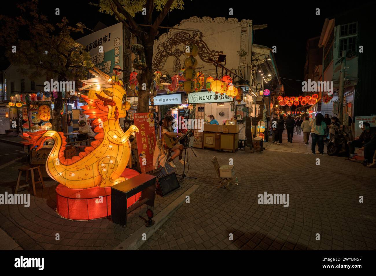 A night scene with a lantern-adorned street celebrating Asian culture, featuring a striking dragon sculpture Stock Photo