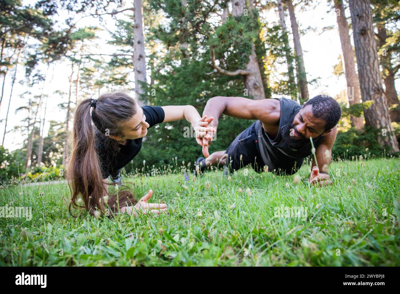 A man and a woman are doing a plank exercise on a grassy field. The man is wearing a black shirt and the woman is wearing a black shirt Stock Photo
