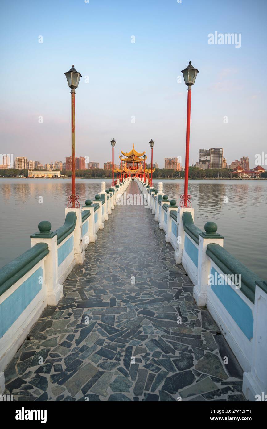 A serene and picturesque view of a stone-paved pier extending over calm waters towards a Chinese pagoda under a blue sky Stock Photo