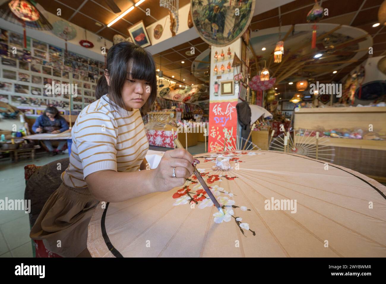 In a workshop, an artist decorates a paper umbrella with intricate floral designs Stock Photo