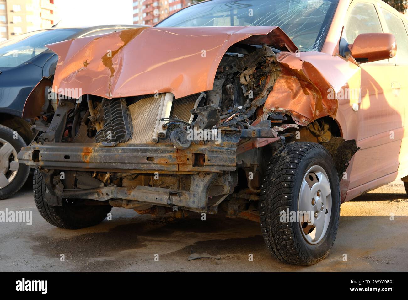 Destroyed car in traffic accident on city road. Smashed broken front of orange auto after crash. Stock Photo
