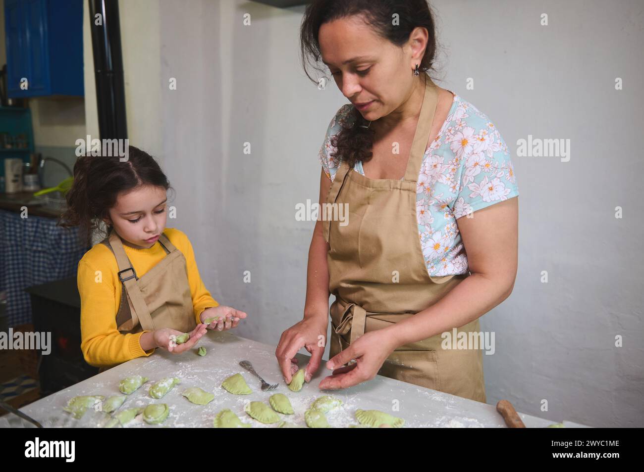 Mother and daughter cooking Ukrainian varennyky in the home kitchen, preparing dinner according to traditional family recipe. People. Culinary. Food a Stock Photo