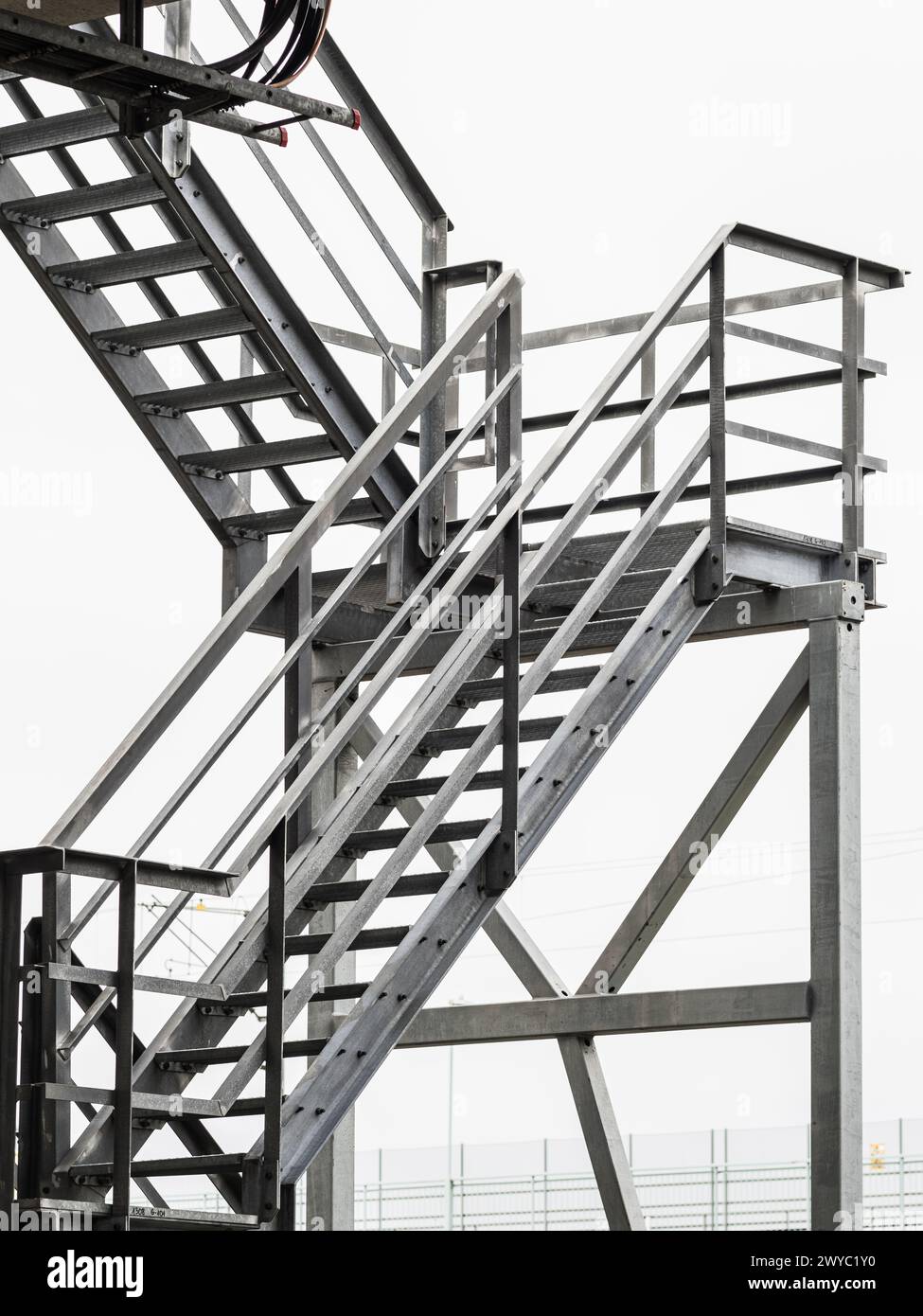 A complex metal staircase ascends against a cloudy sky in Gothenburg, Sweden, featuring multiple platforms and a sturdy construction of steel beams an Stock Photo