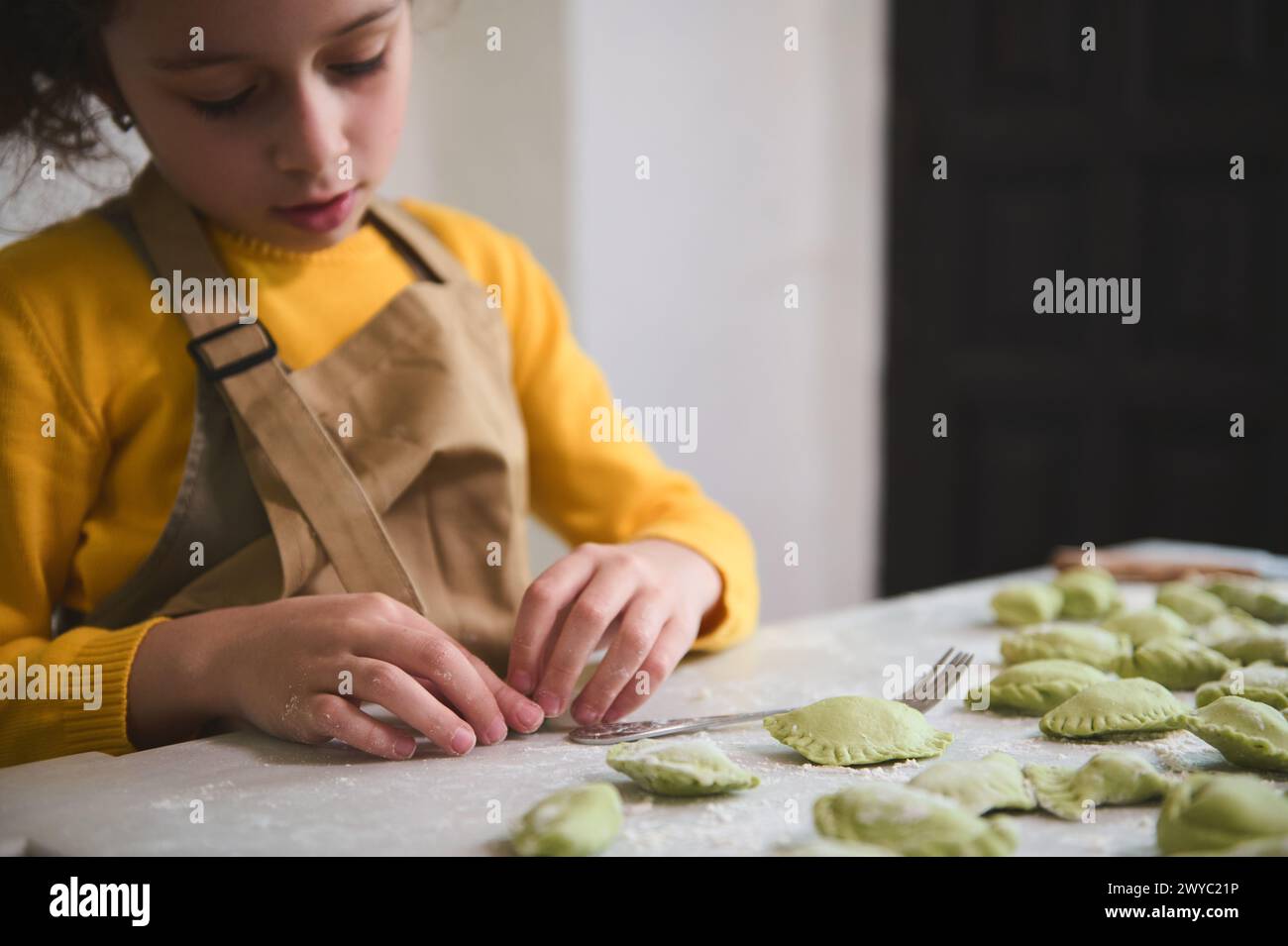 Caucasian adorable little kid girl in the rural kitchen, sculpts dumplings from dough with mashed potatoes filling. Cooking homemade vegetarian dumpli Stock Photo