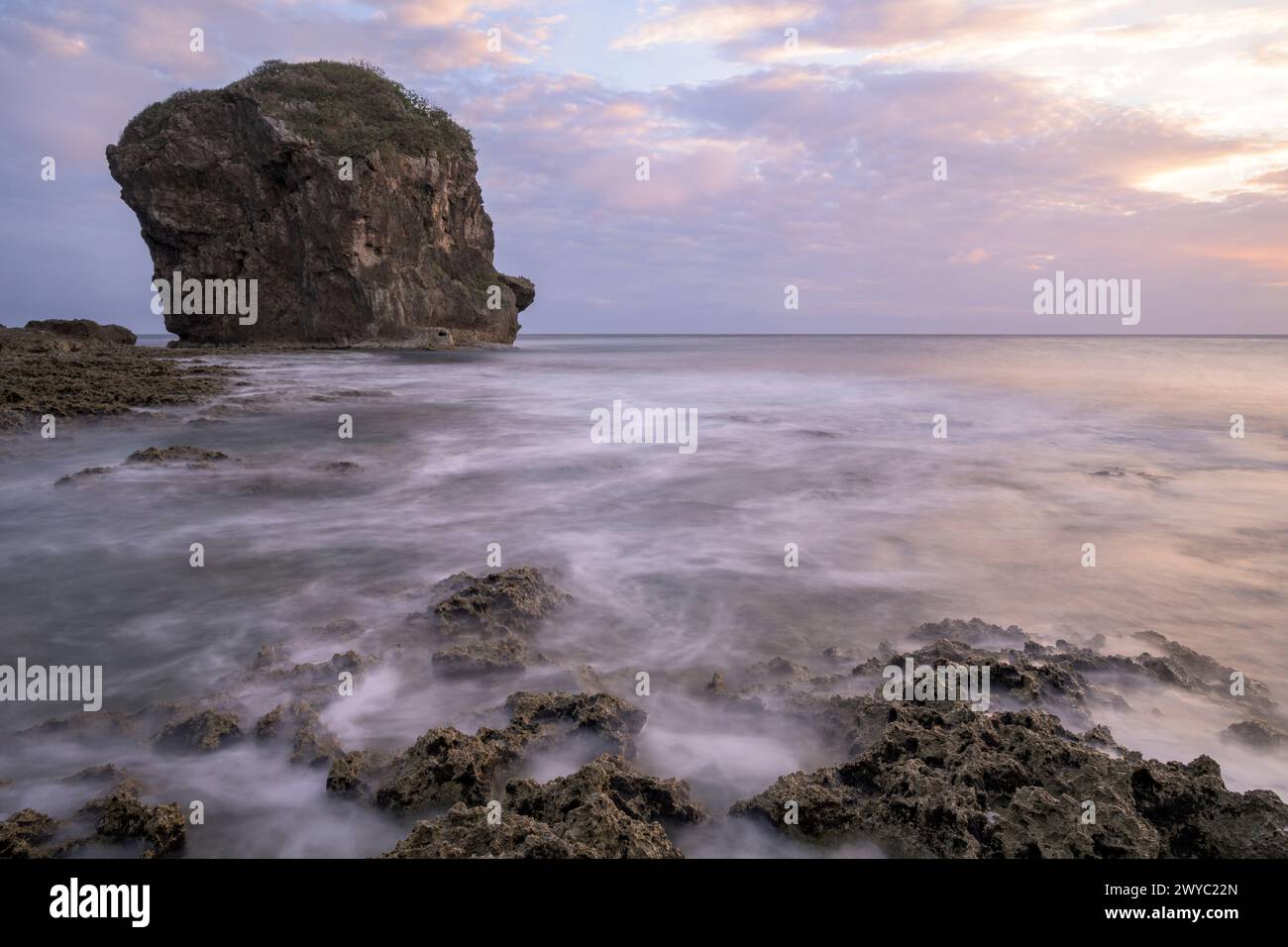 A serene sunset with a rocky outcrop standing tall amid a silky sea with a long exposure effect Stock Photo