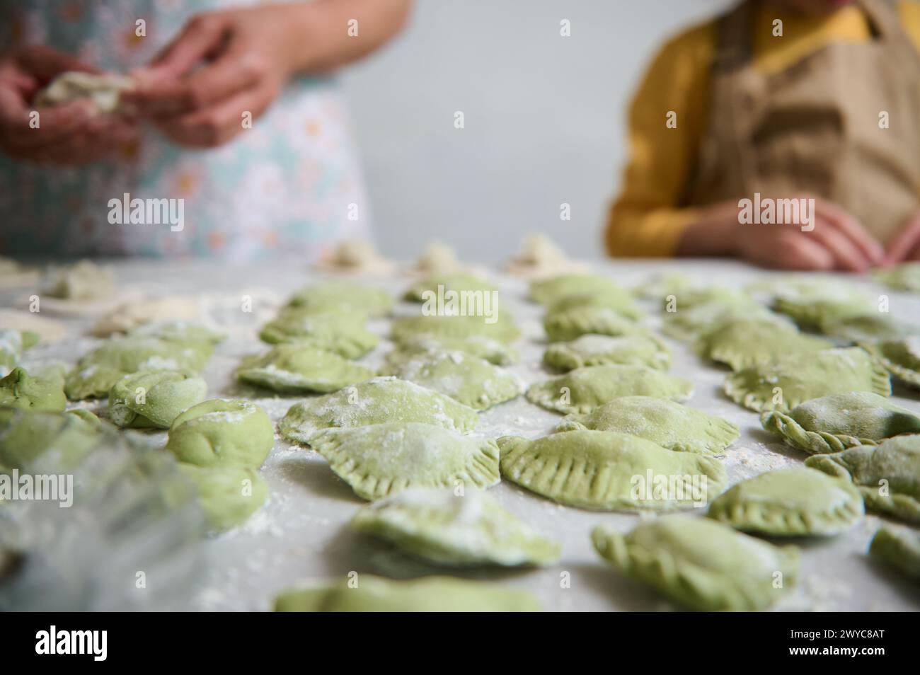 Selective focus on molded homemade dumplings on floured table, against the background of young mom and daughter cooking together. Ravioli. Pelmeni. Va Stock Photo