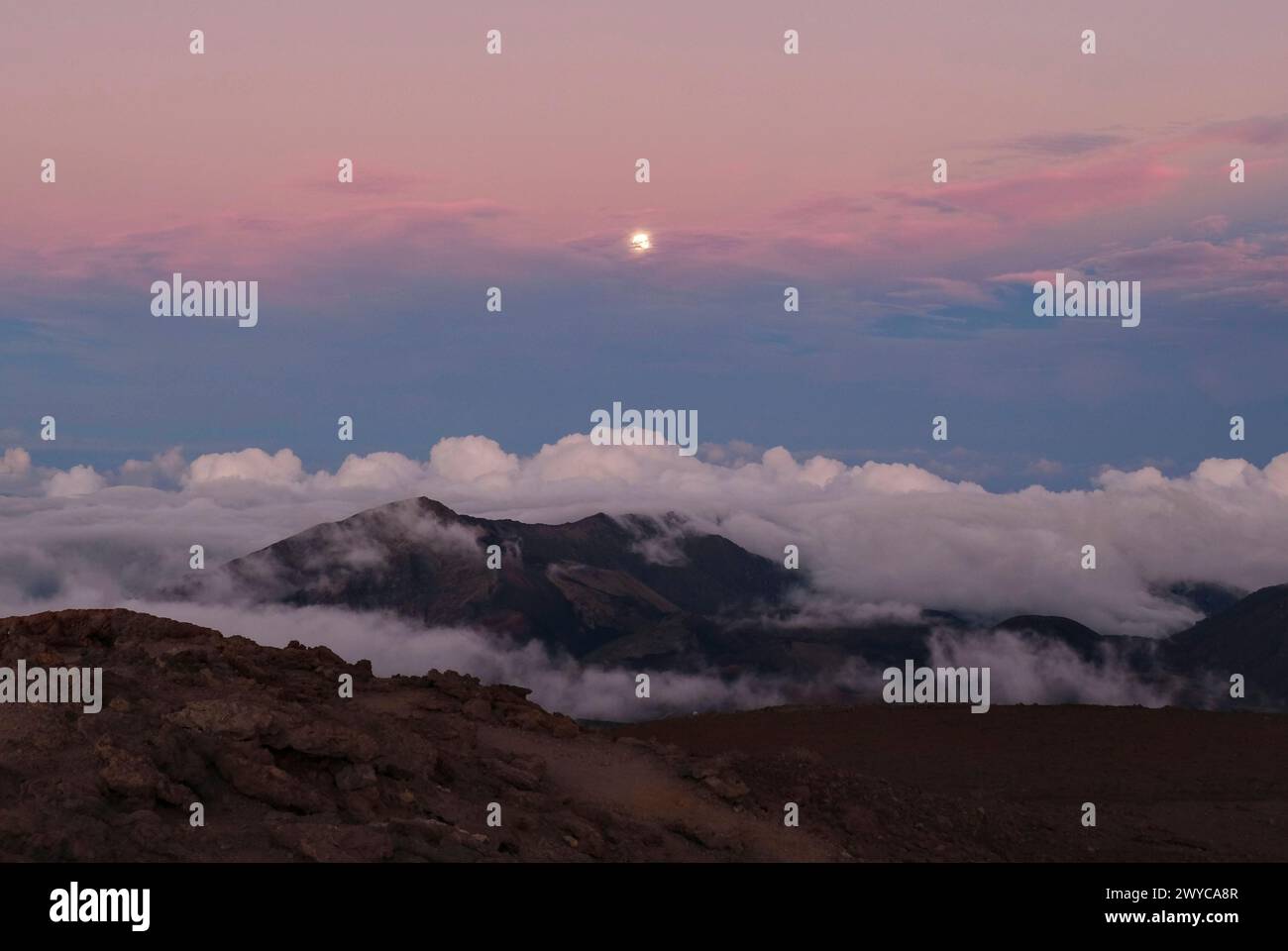 A moonrise after sunset with clouds rolling over the mountains Stock Photo