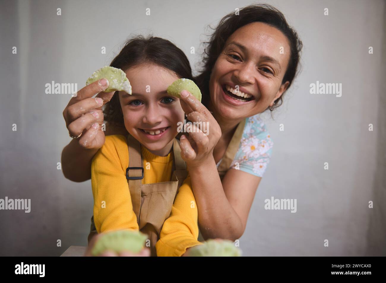 Close-up portrait of a mother and daughter having fun, smiling looking at camera, holding molded dumplings in the home kitchen. Mother and daughter co Stock Photo