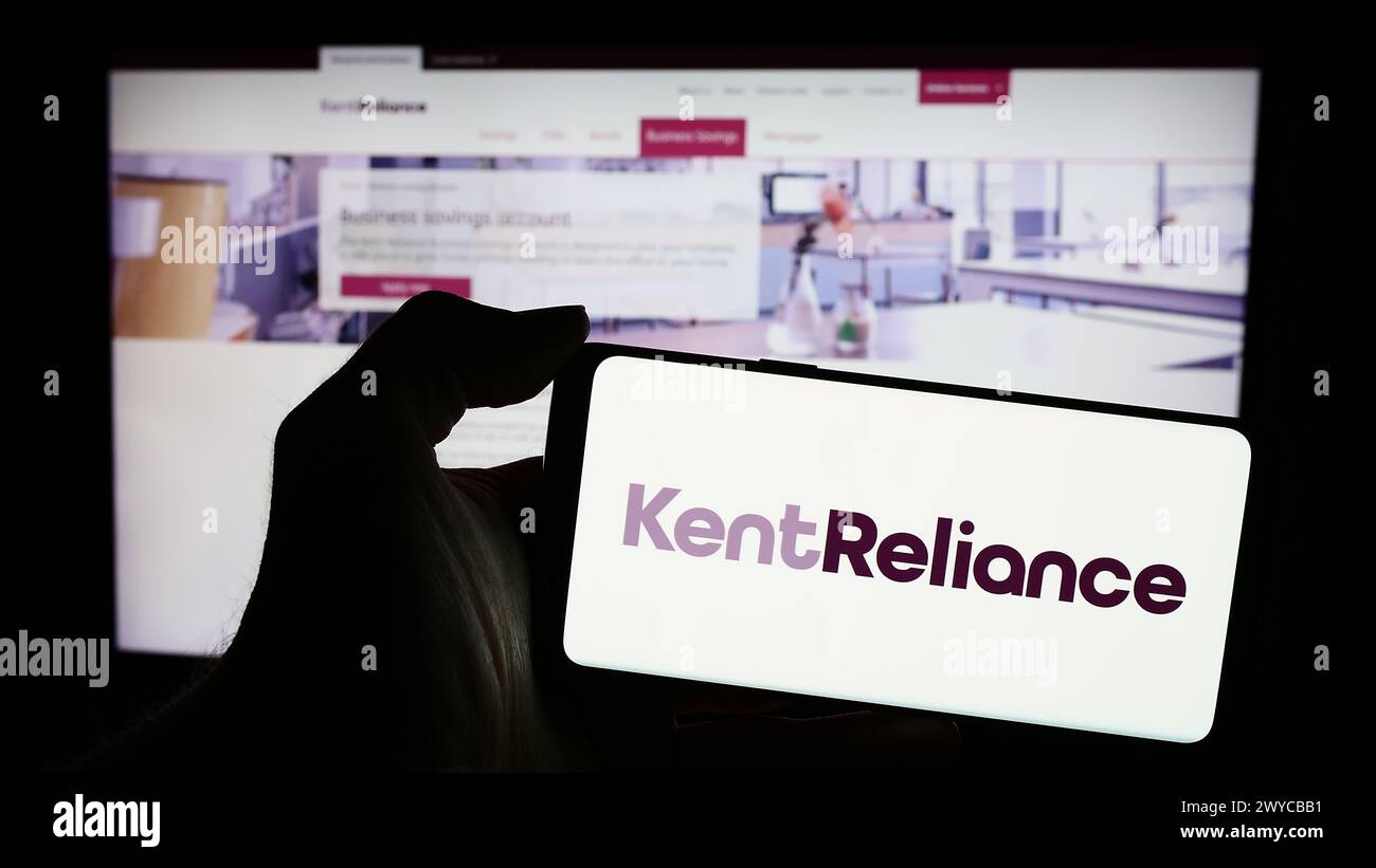 Person holding mobile phone with logo of British financial services company Kent Reliance in front of business web page. Focus on phone display. Stock Photo