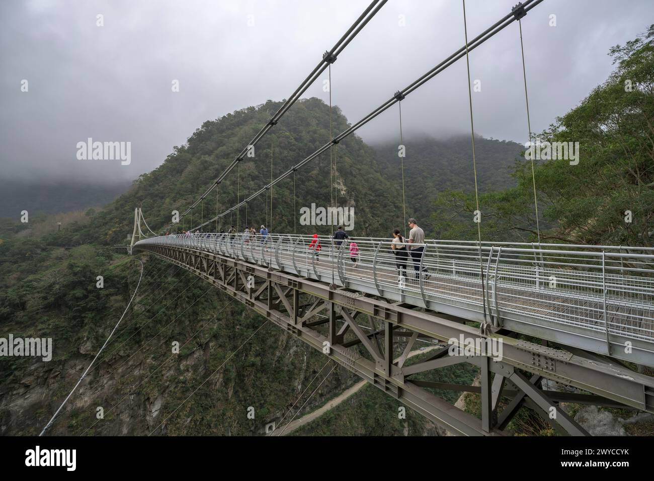 People cross a modern suspension bridge enveloped by fog in a mountainous landscape over Taroko gorge Stock Photo