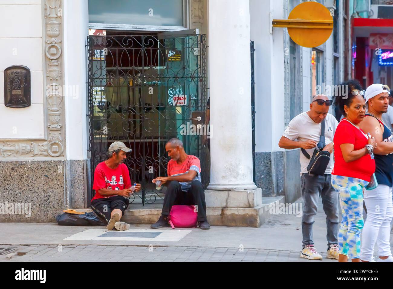 Two Cuban men drinking alcohol on a doorstep of building, other people ...