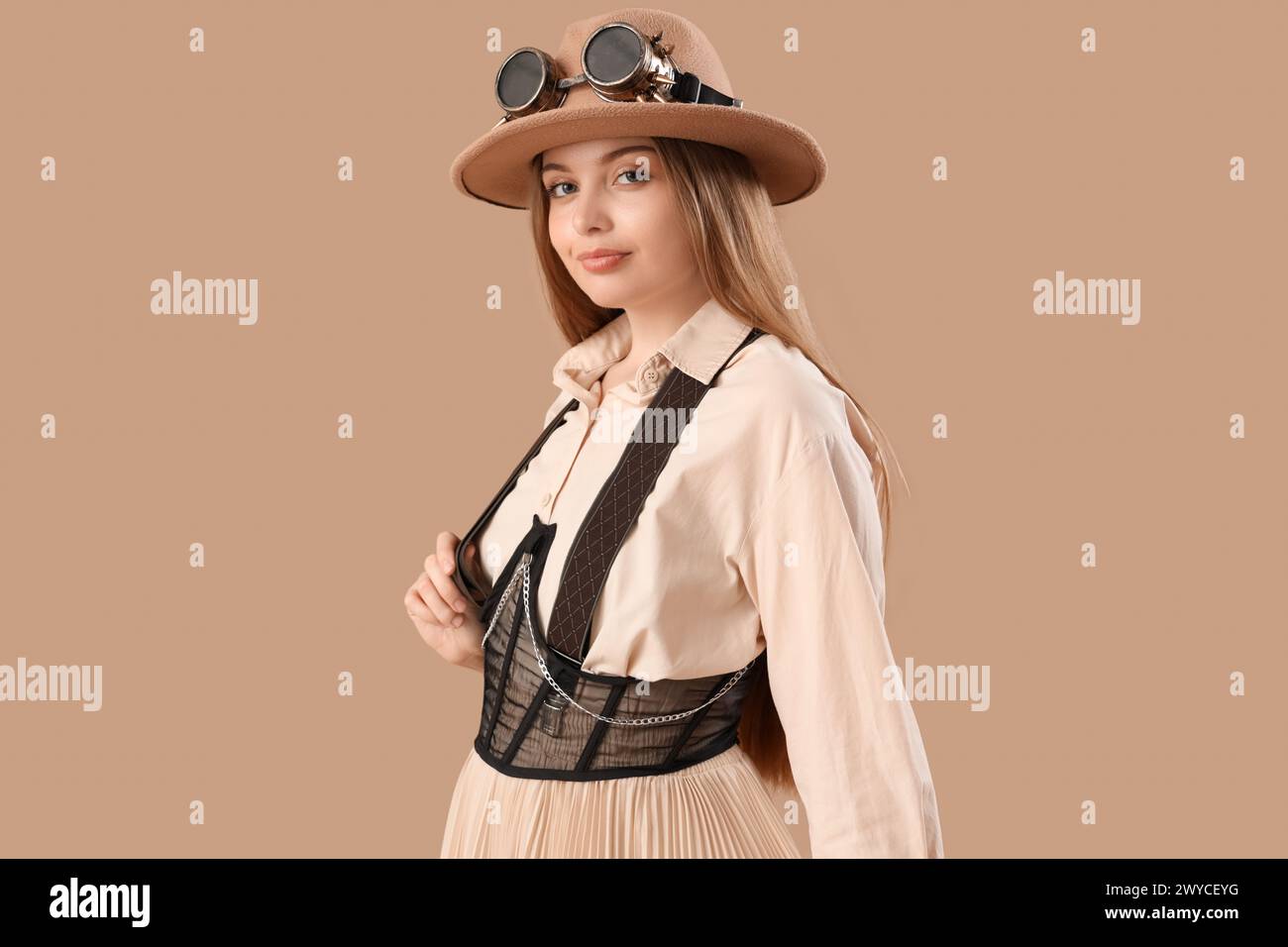 Stylish young woman in steampunk goggles on beige background Stock Photo