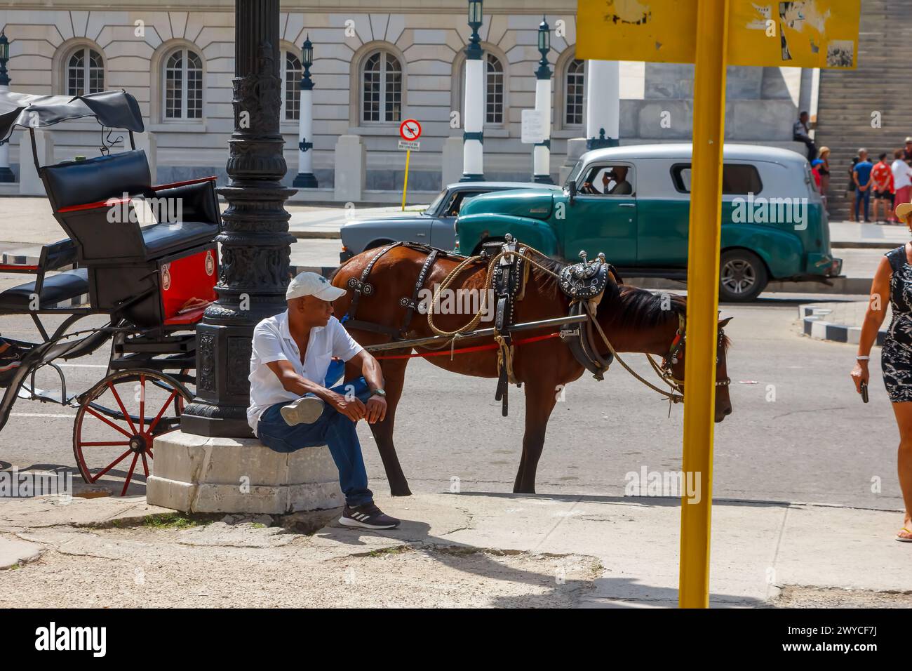 Cuban man sitting on an old light pole, horse carriage and vintage car in Havana, Cuba Stock Photo