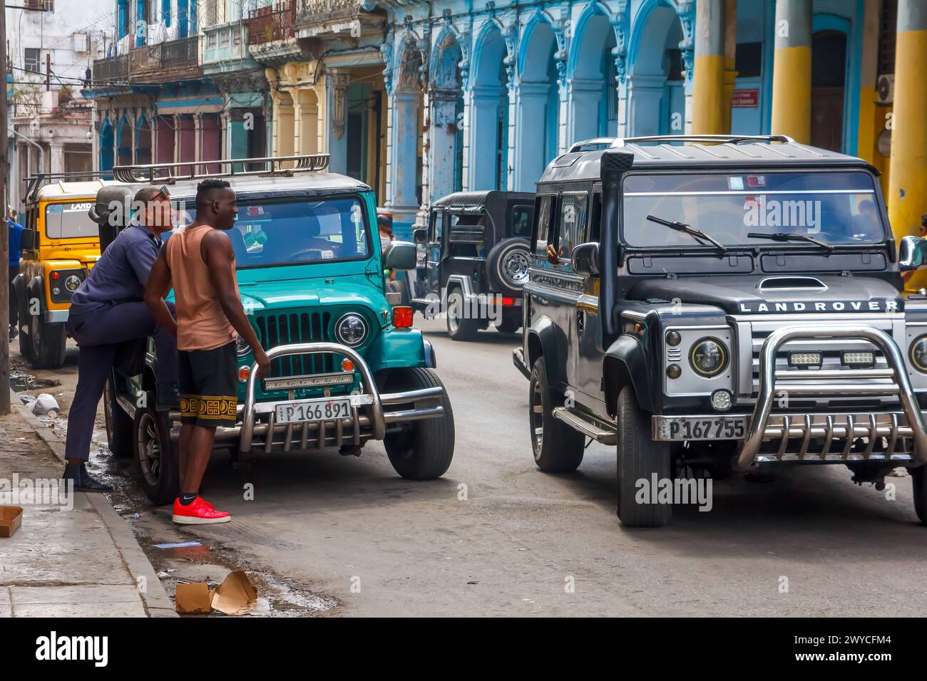 Cuban man by an old jeep, other vehicles in the city street in Havana, Cuba Stock Photo