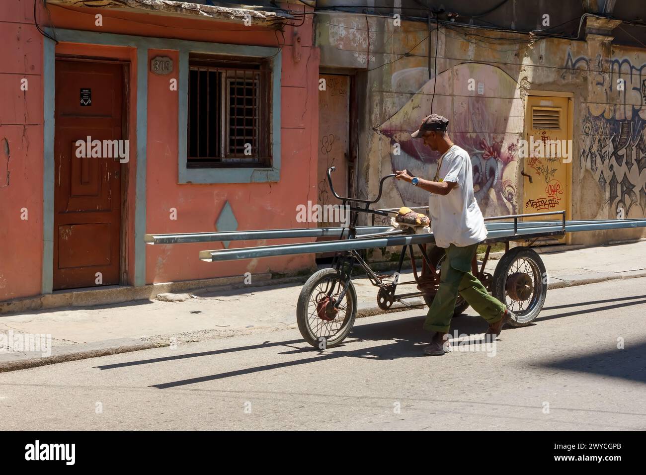 Cuban man pushing tricycle with construction beams in Havana, Cuba Stock Photo