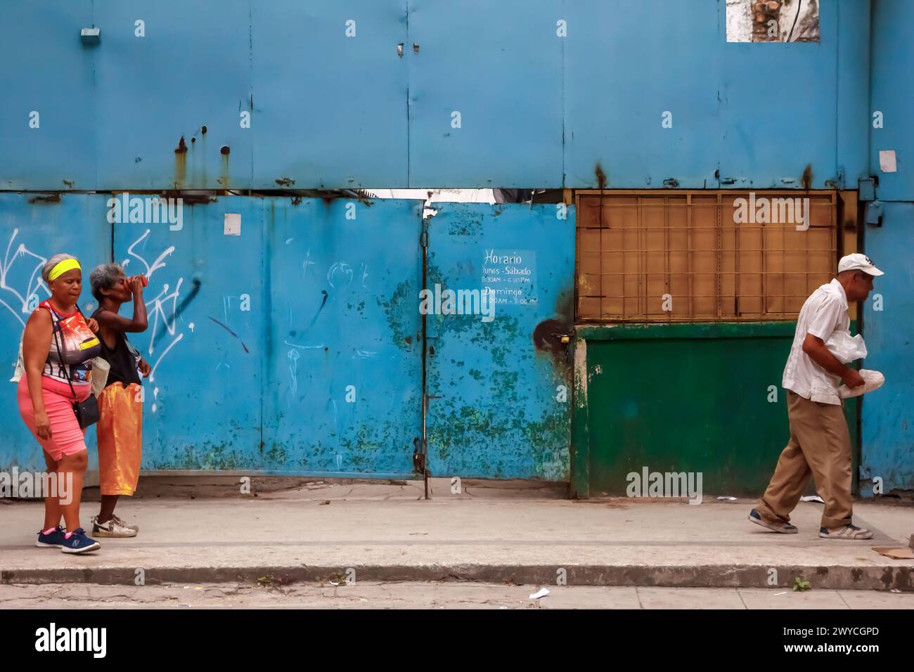 Cuban people walking by dirty metal door and building facade in Havana, Cuba Stock Photo