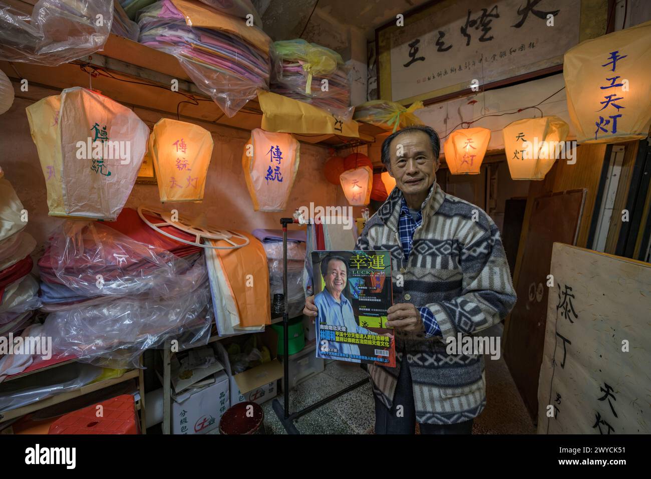 Elderly man proudly displaying traditional paper lanterns at an old shop Stock Photo