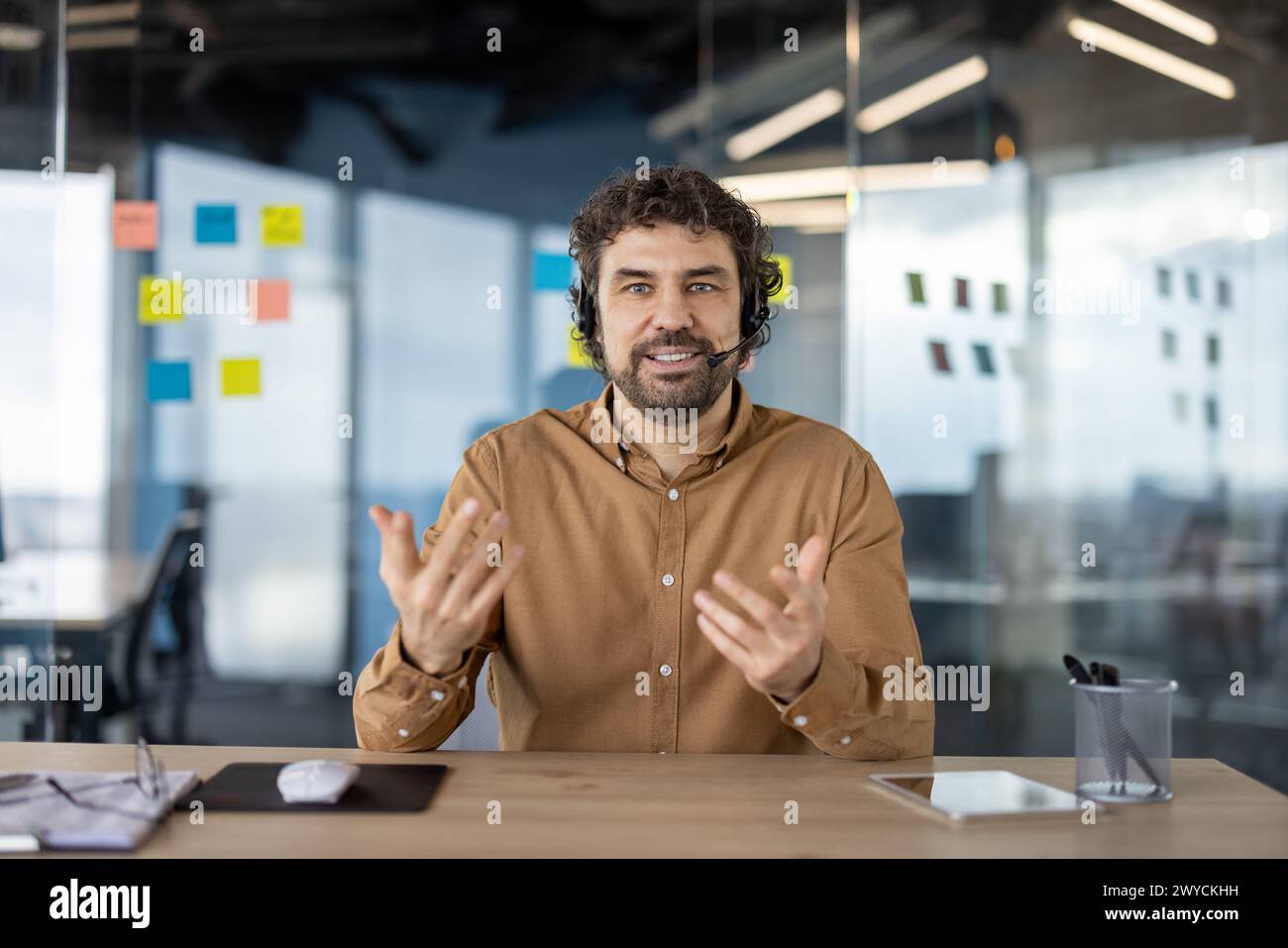 Smiling male professional with headset engaging in a business conversation in a contemporary workspace with sticky notes in background. Stock Photo