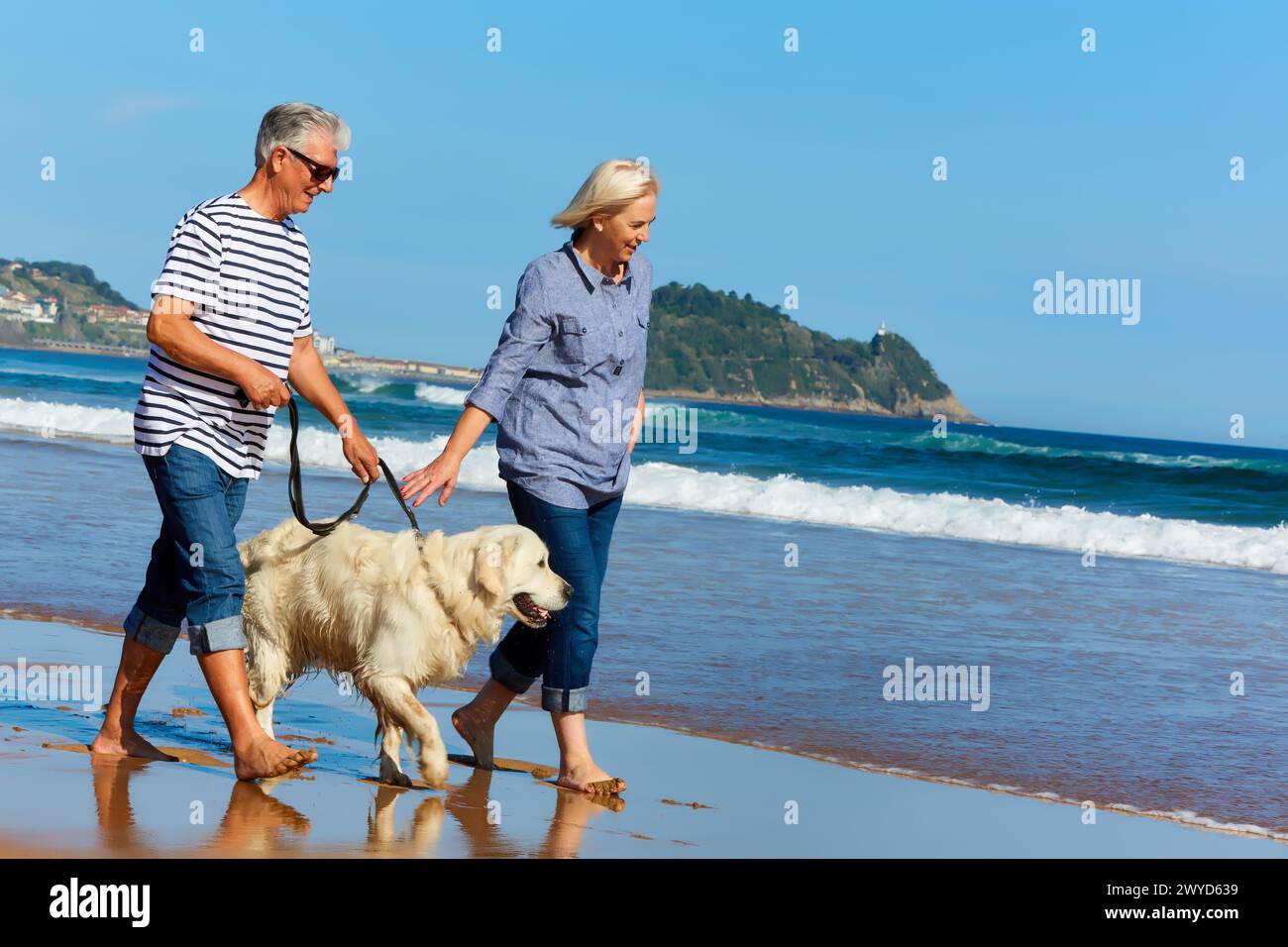 Senior couple, 60-70, Walking with dog on the beach, background Getaria, Zarautz, Gipuzkoa, Basque Country, Spain, Europe. Stock Photo