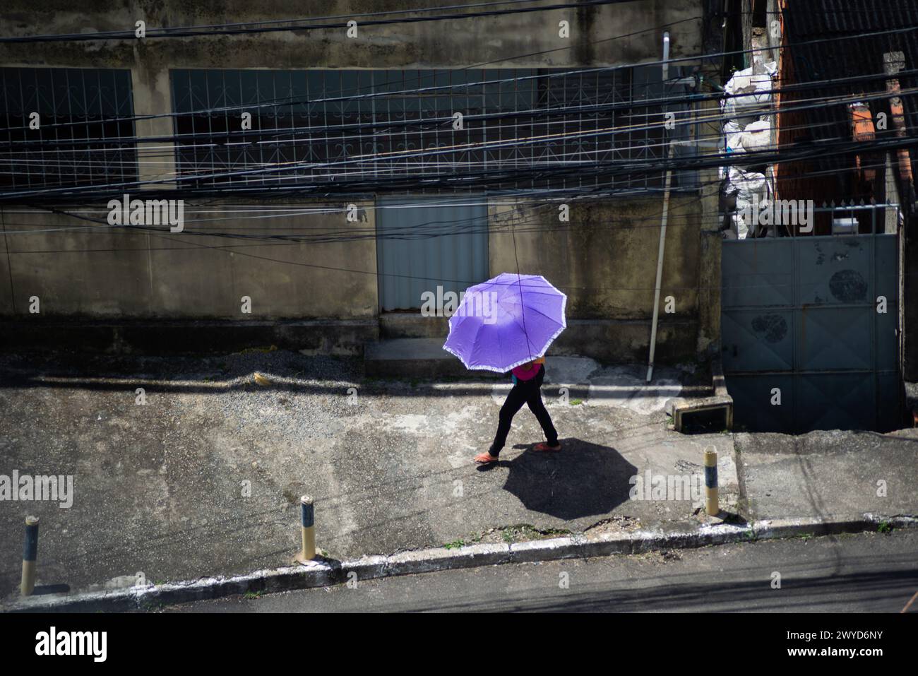 Salvador, Bahia, Brazil - January 28, 2022: A pedestrian is seen walking down the street with an umbrella to protect himself from the strong sun in th Stock Photo