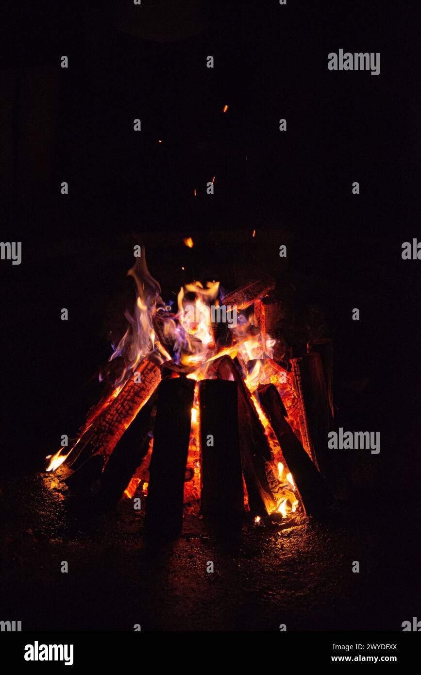 A campfire burns brightly in the darkness, with vivid orange flames and ...