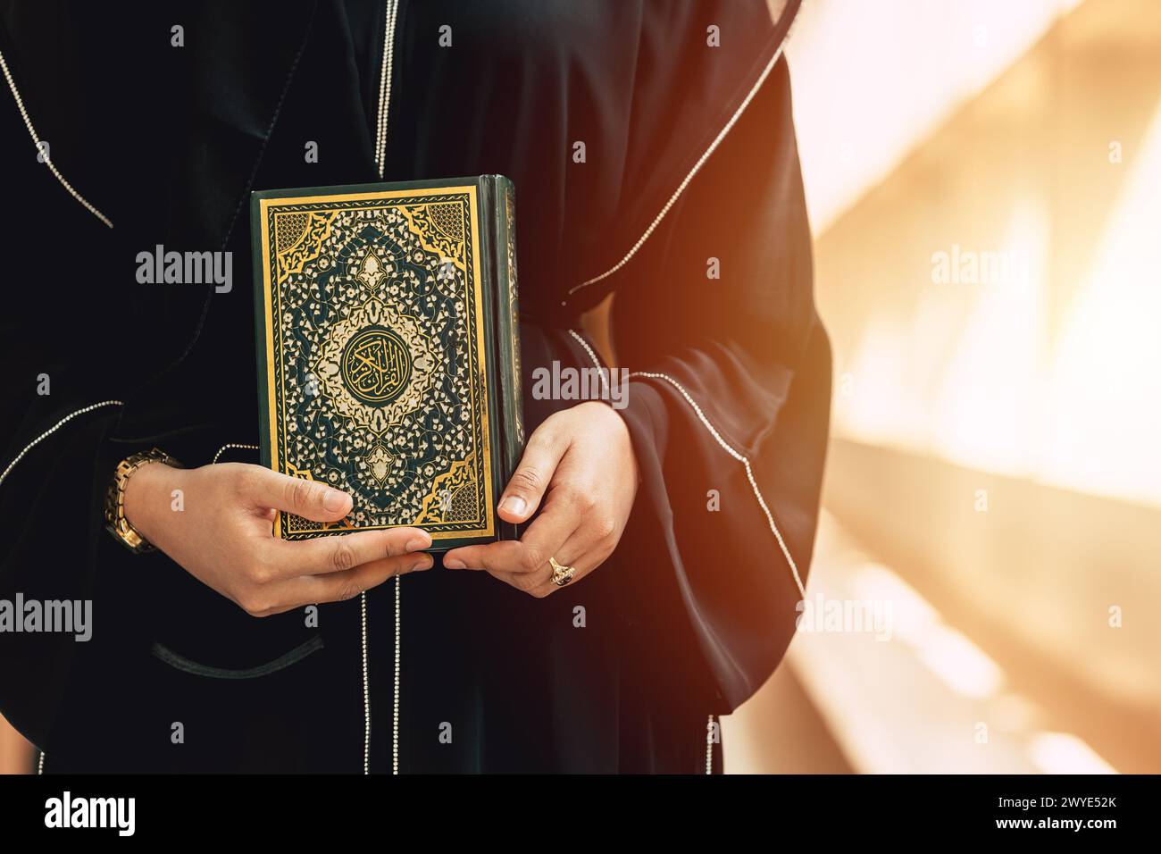 Holy Quran book cover with arabic calligraphy translate meaning of Al Quran. Closeup Arab people hand holding Quran muslim book. Stock Photo