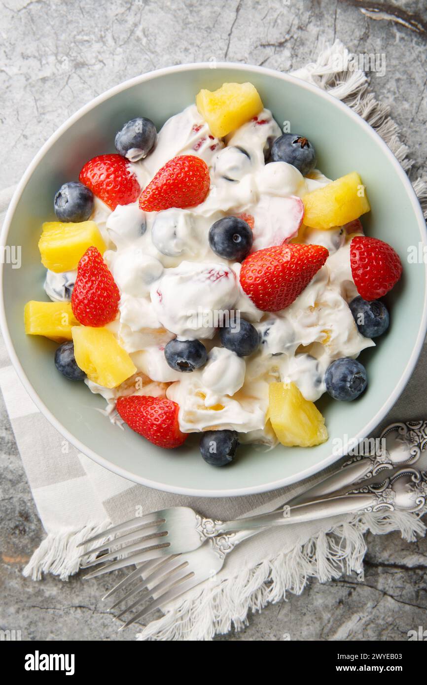 Delicious cheesecake fruit and berry salad with strawberries, blueberries, pineapple close-up in a bowl on a marble table. Vertical top view from abov Stock Photo
