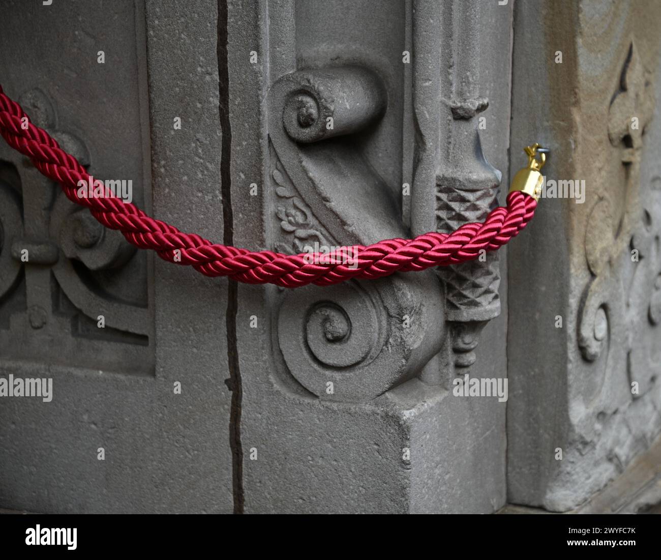 Elegant crowd control twisted fuchsia stanchion rope with polished gold hooks against an antique stone wall in Riquewihr, Alsace, France. Stock Photo