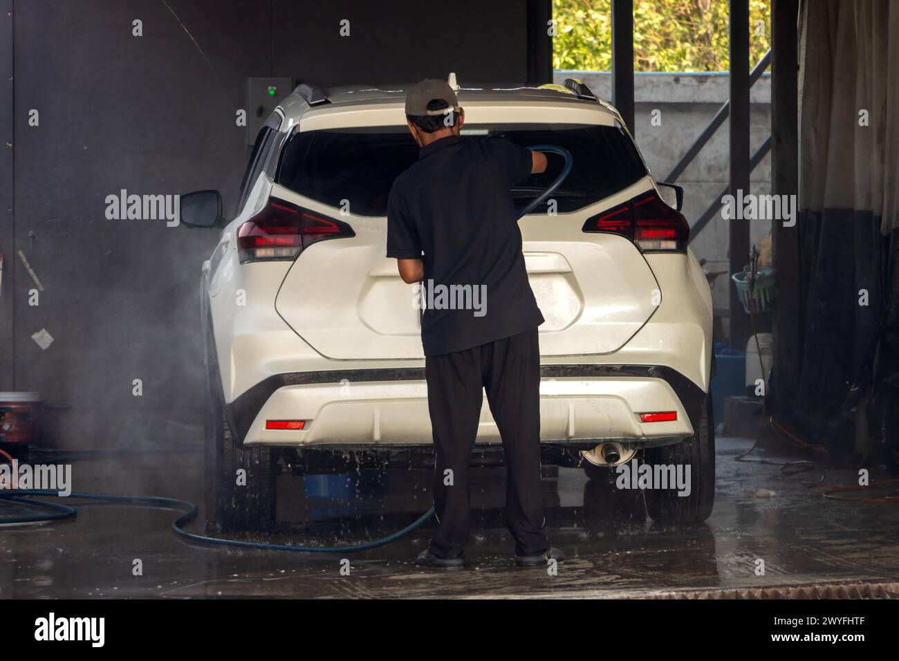 A man washes a car with a pressure hose inside a service station Stock Photo