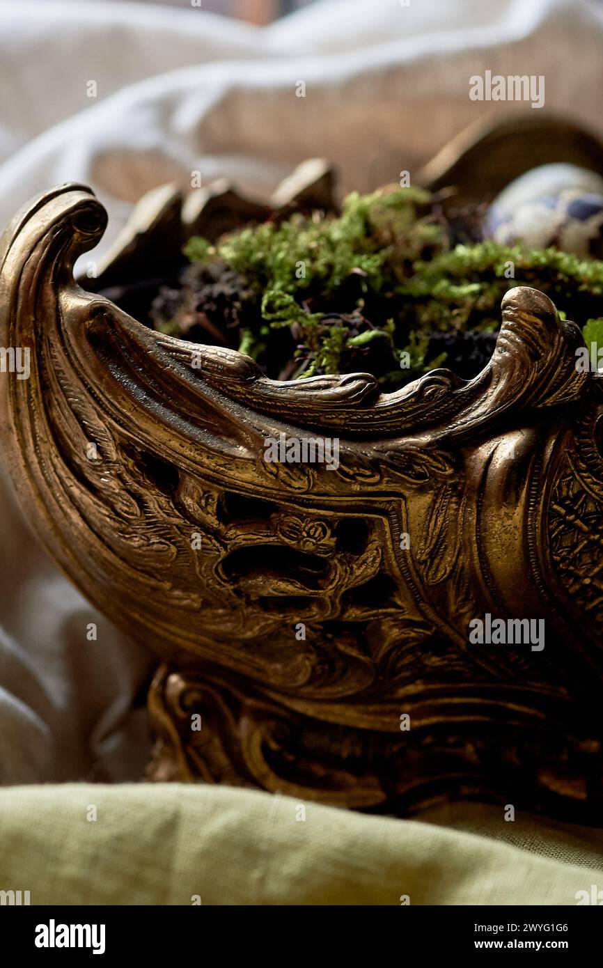 A massive bronze vase on legs with moss, greenery sprouted in an egg. A new life Stock Photo