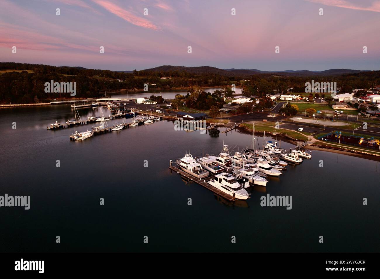 A beautiful pink sunset over Saint Helen's harbour Tasmania with boats docked on calm waters. Stock Photo