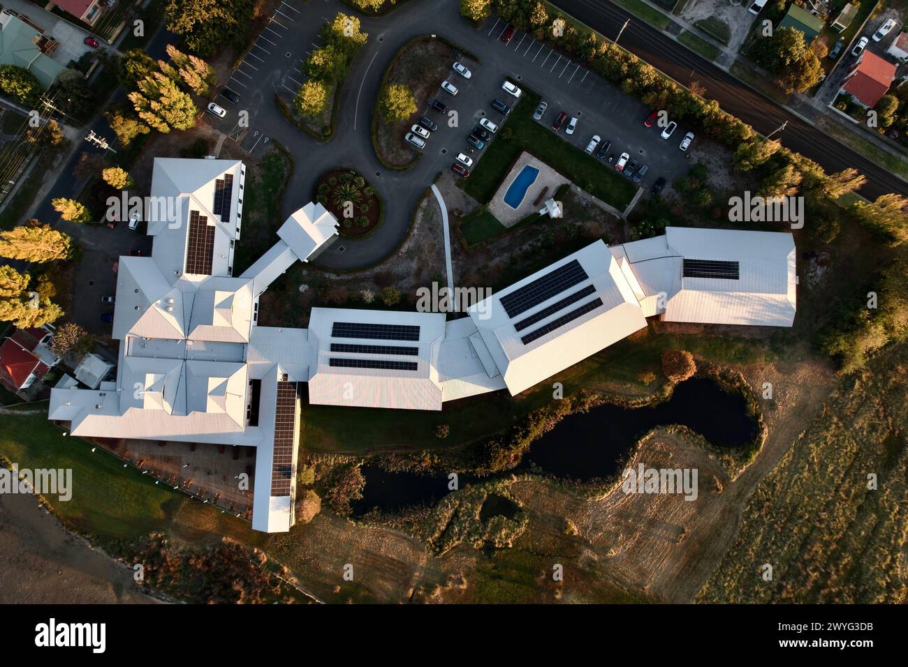A White roof environmentally friendly hotel with a lake, pool and car park, aerial top down. Stock Photo