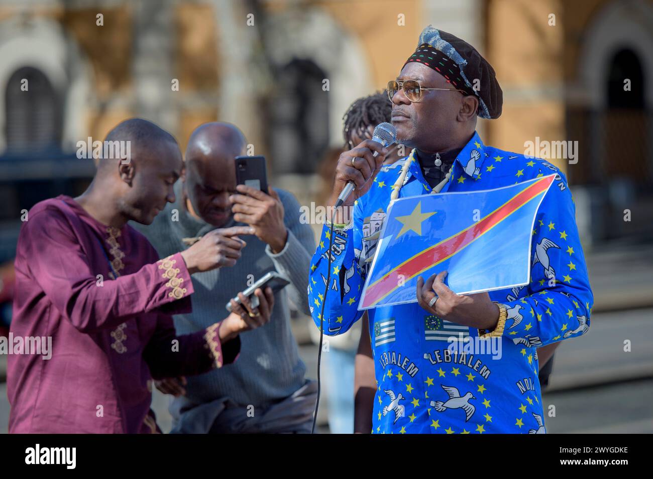 April 6, 2024, Rome, Italy: A man displays the Congo flag while speaking into the microphone during the demonstration to express solidarity with the Congolese people, to ask for a 'stop to the ongoing genocide' and an end to the exploitation of the African continent organized by some associations of the African communities of Europe together with the Communist Network and the Hands Off from Africa movement in Rome.According to the organizers, the 30 years of armed conflict financed by the Western war industry have caused the death of 15 million civilians and 7 million displaced people in one o Stock Photo