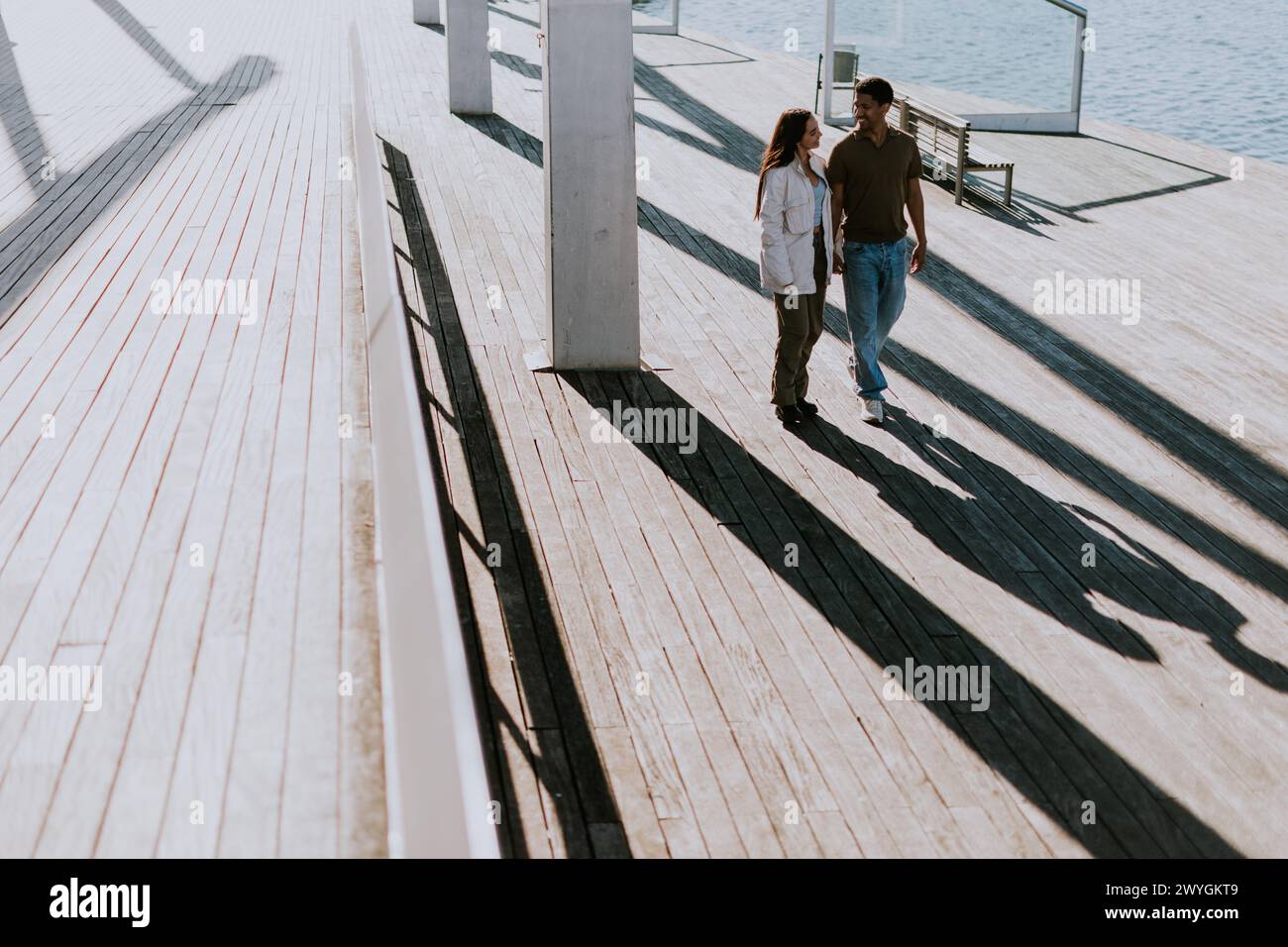 Young couple walks hand in hand, casting long shadows on the wooden ...