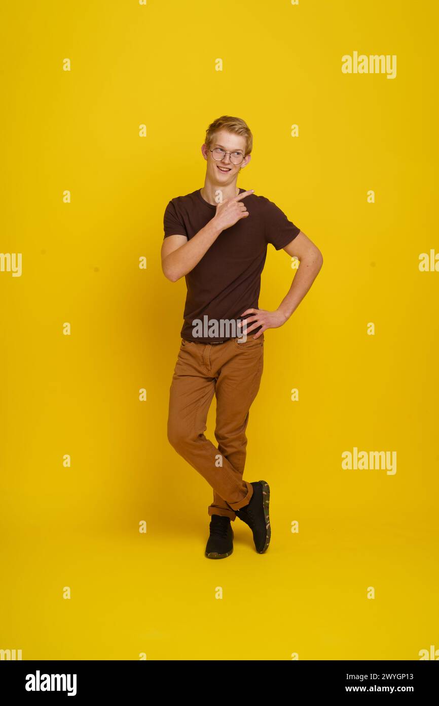 A young man in a brown shirt and tan pants is posing for a photo in front of a yellow background Stock Photo