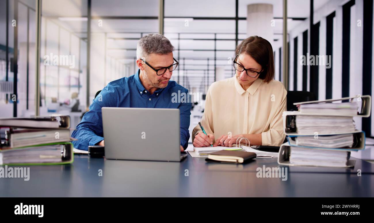 Two Businesspeople Calculating Invoice In Office While Using Laptop Stock Photo