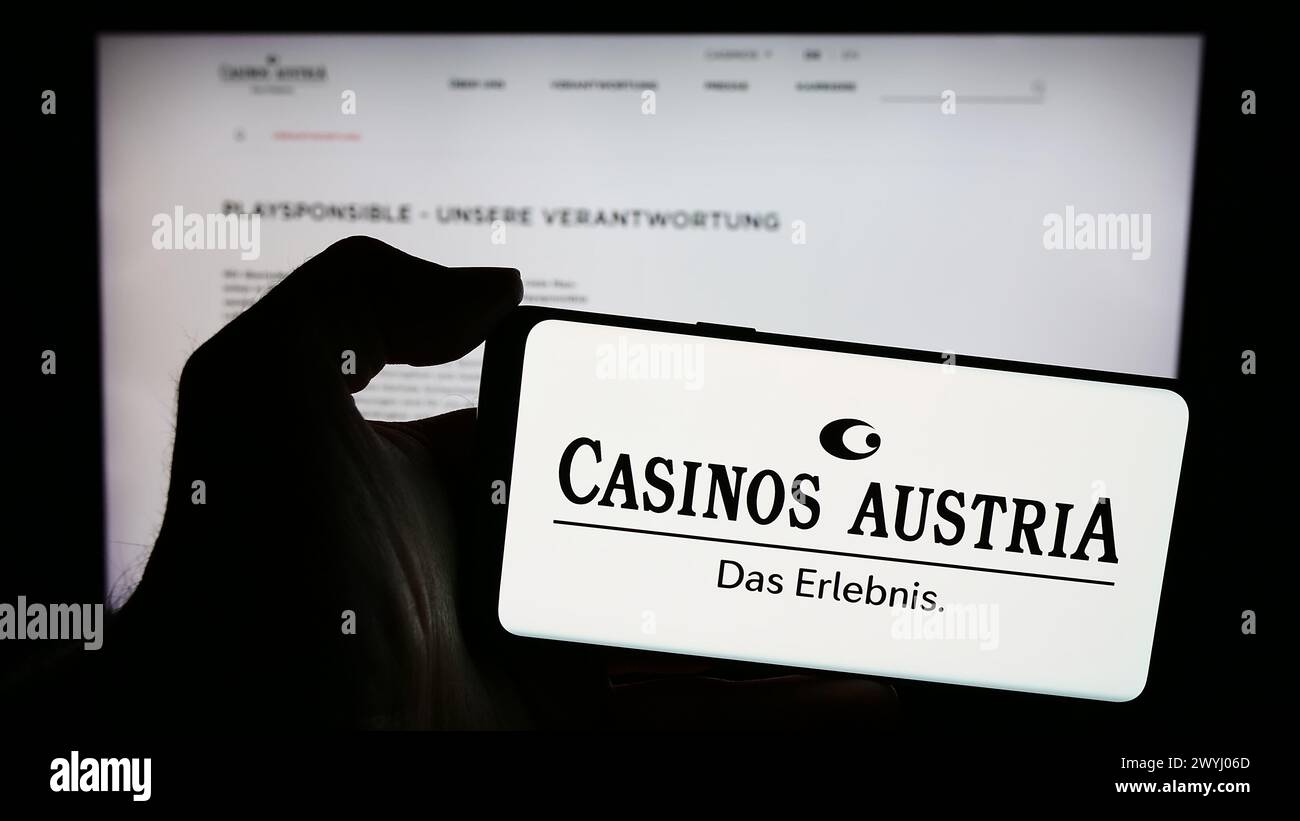 Person holding mobile phone with logo of Austrian gambling company Casinos Austria AG in front of business web page. Focus on phone display. Stock Photo