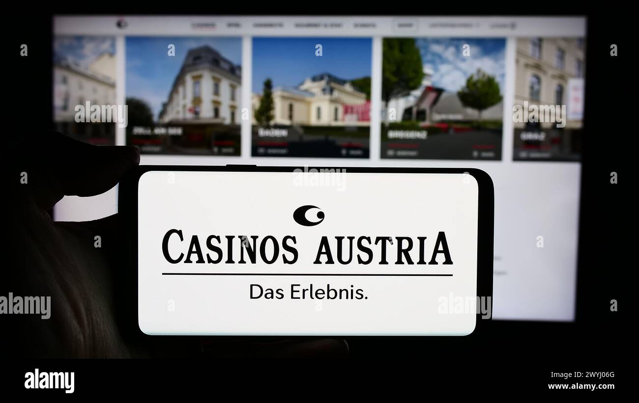 Person holding cellphone with logo of Austrian gambling company Casinos Austria AG in front of business webpage. Focus on phone display. Stock Photo