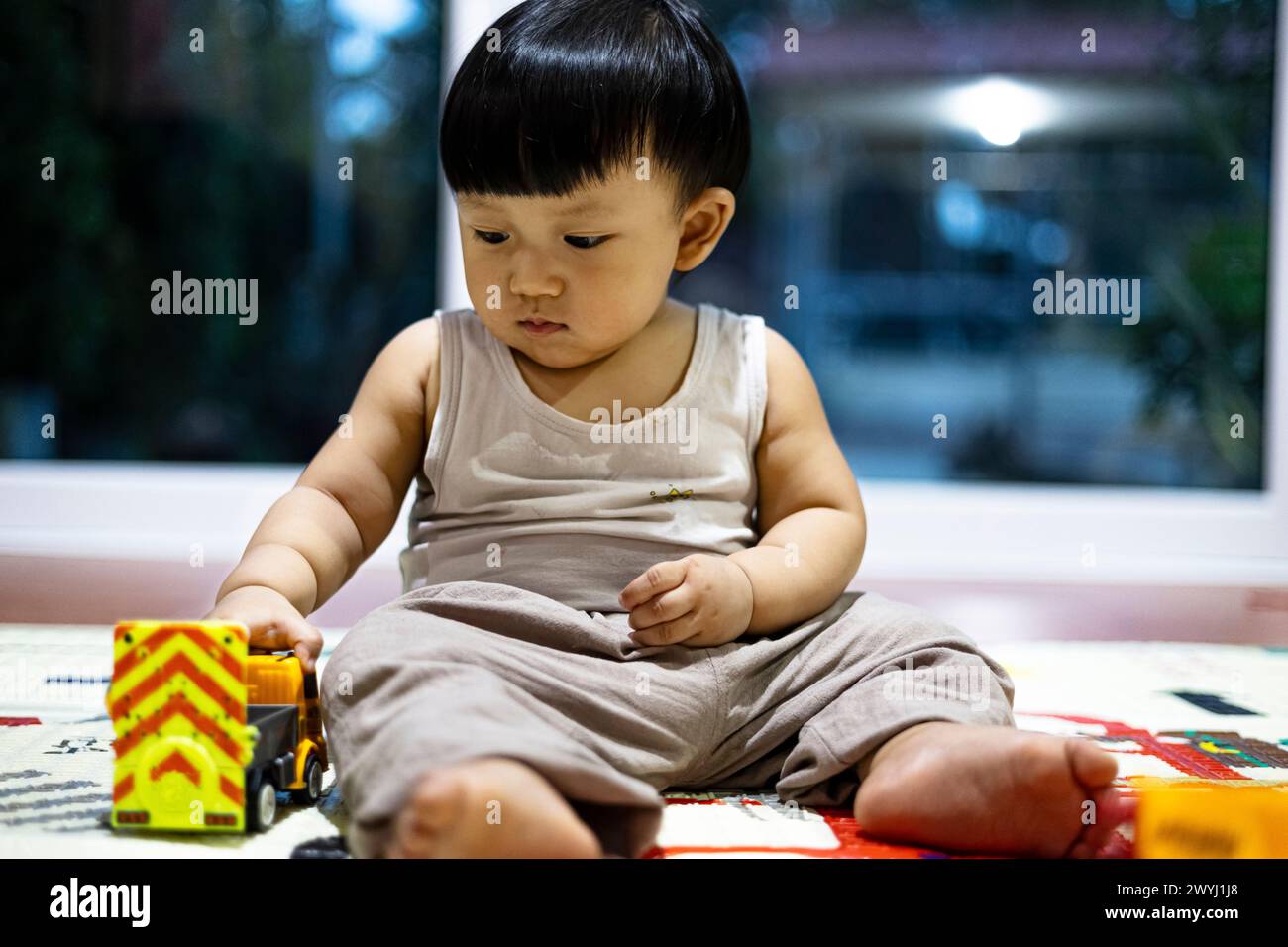 Close up of little boy in casual clothes sitting on floor and playing toy trucks while spending free time at home. Stock Photo