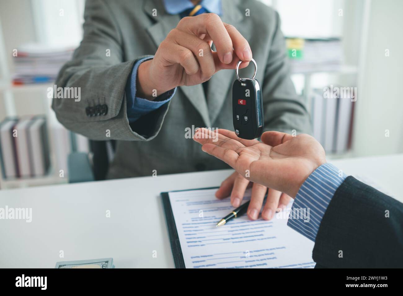 car dealer is handing over car keys to customer after sales contract and installment contract have been signed. Concept of handing over car keys to cu Stock Photo