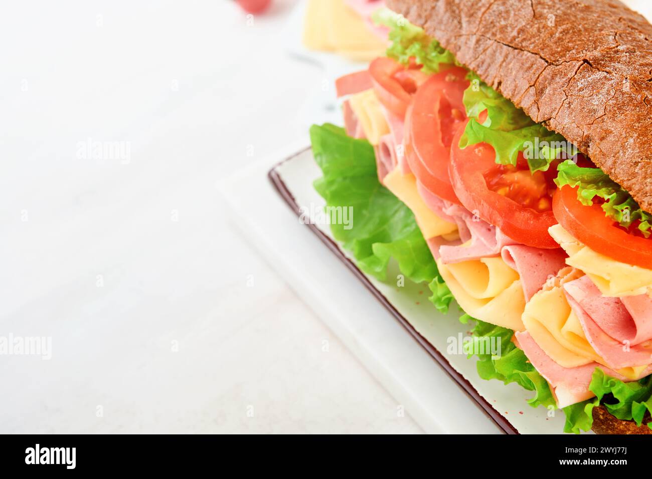 Sandwich. One fresh big submarine sandwich with ham, cheese, lettuce, tomatoes and microgreens on light background. Healthy breakfast theme concept, s Stock Photo