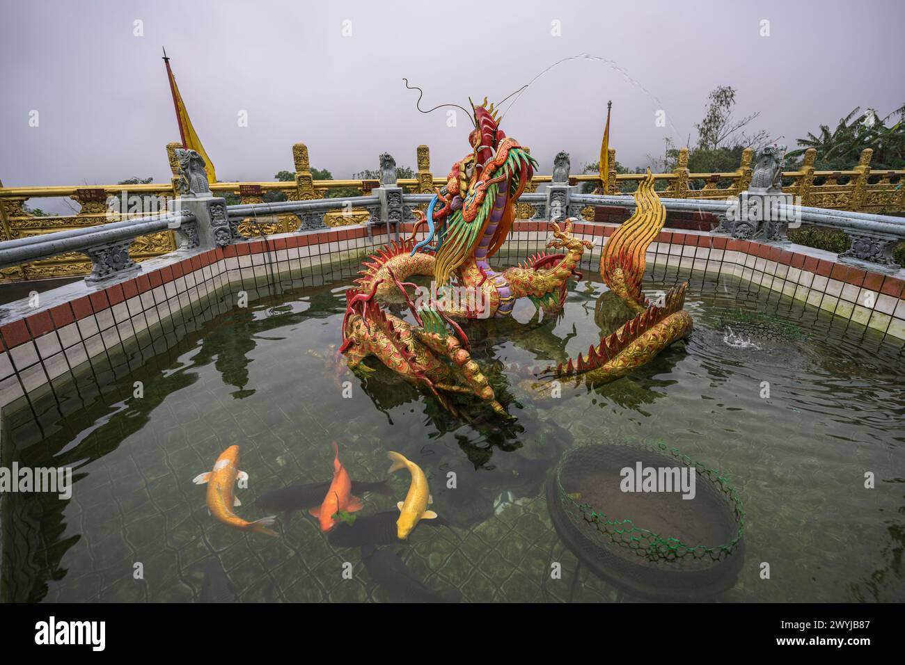 A colorful dragon statue emerges from a misty pond where there are colourful carps Stock Photo