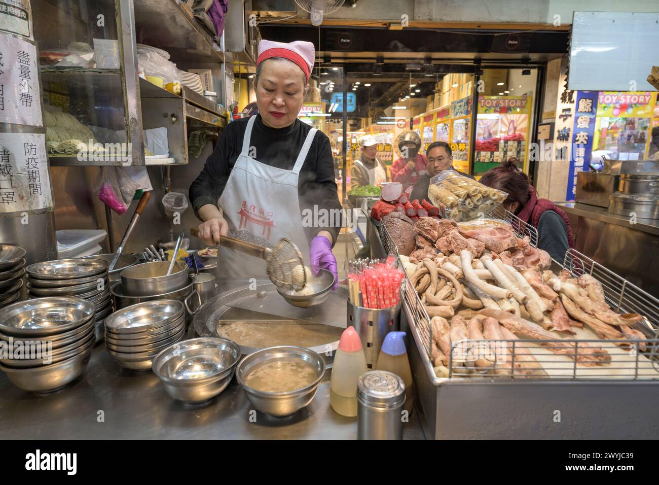 A street vendor attentively prepares a dish by the roadside with a variety of meat on display Stock Photo